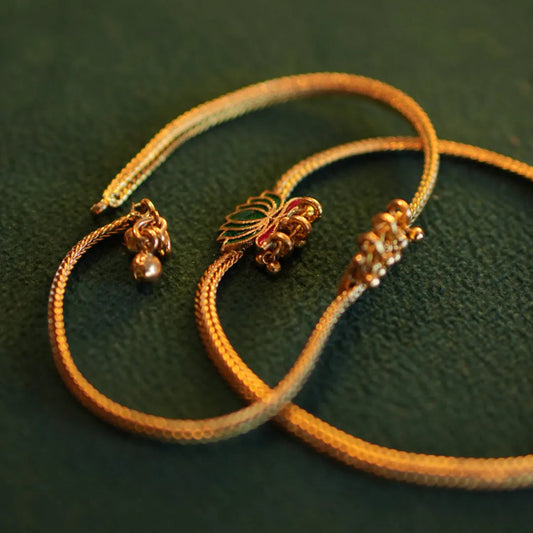 Two gold bracelets with decorative ends on a green background