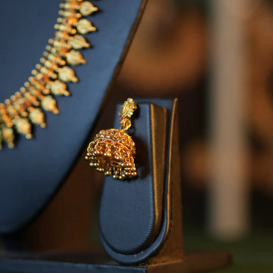 Gold necklace and earring set on a blue stand with a blurred background