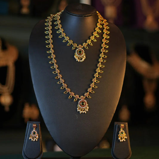 Gold necklace and earrings on a black mannequin bust with a blurred jewelry store background.