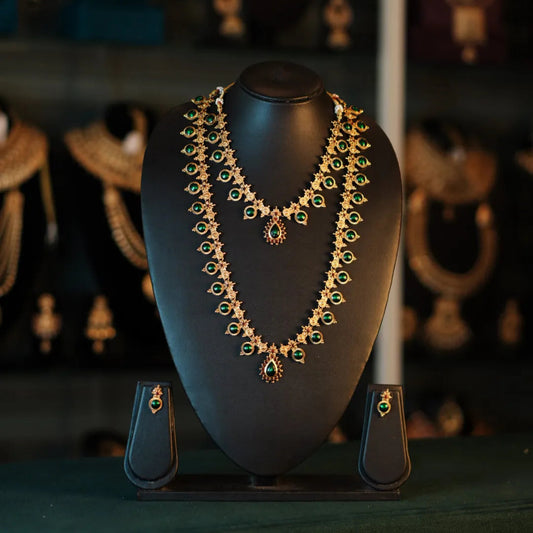 Gold and green necklace on a black mannequin bust with blurred jewelry in the background