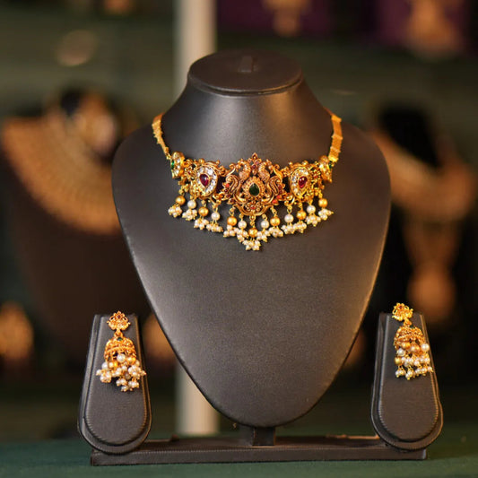 Gold necklace and earrings set on a black mannequin bust with a blurred jewelry store background.