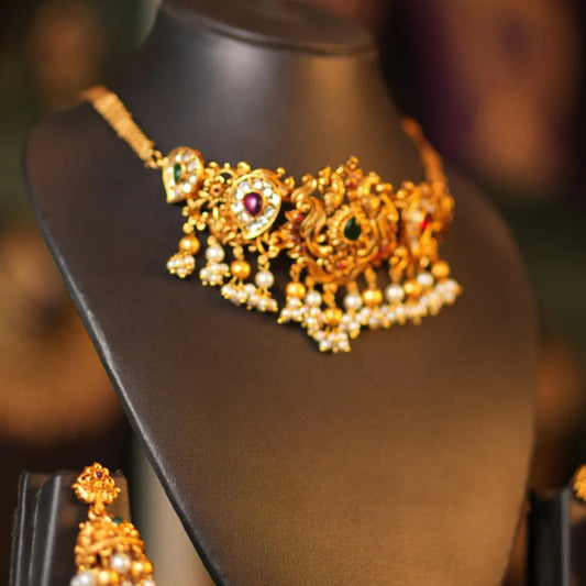 Gold necklace with a red gemstone on a mannequin bust against a blurred background