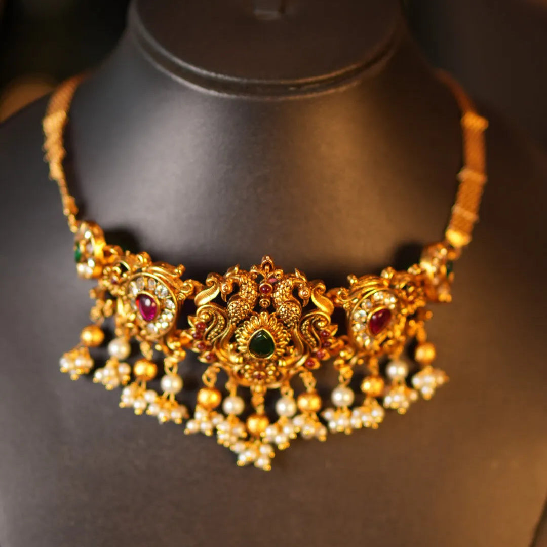 Gold necklace with intricate designs on a black mannequin bust.