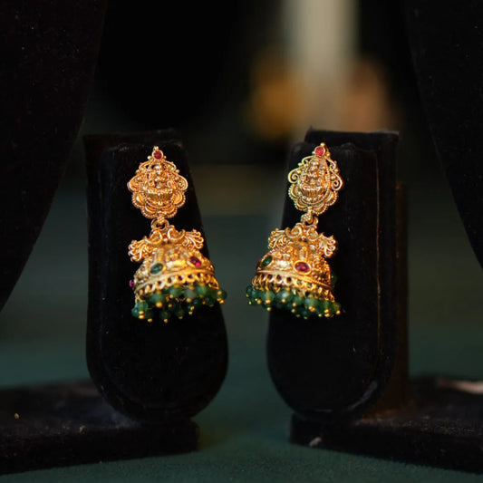 Gold earrings with green gemstones on a dark background