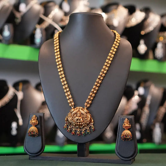 Gold necklace and earrings on a mannequin bust with a blurred jewelry store background.