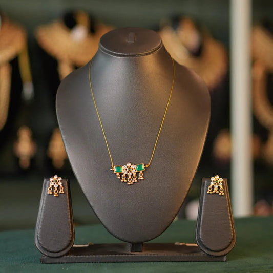 Gold necklace with green stones on a black jewelry stand with blurred earrings in the background.
