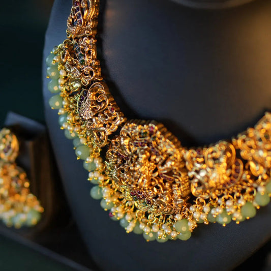 Gold necklace with green beads on a black stand