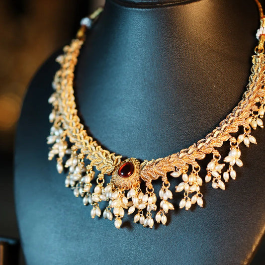 Gold necklace with pearls and a red gemstone on a black mannequin.