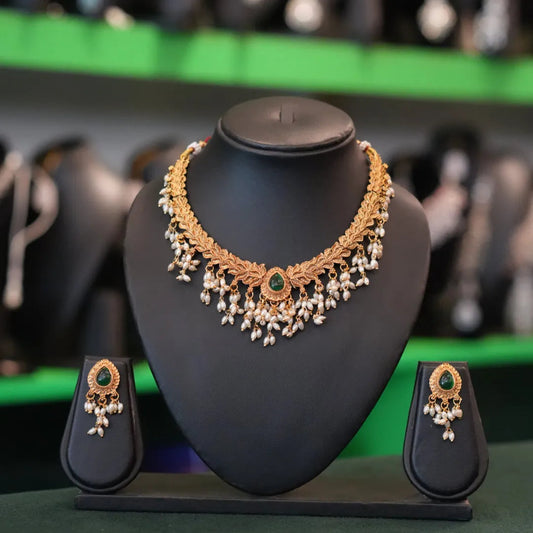 Gold necklace and earrings set on a black stand with blurred shoes in the background