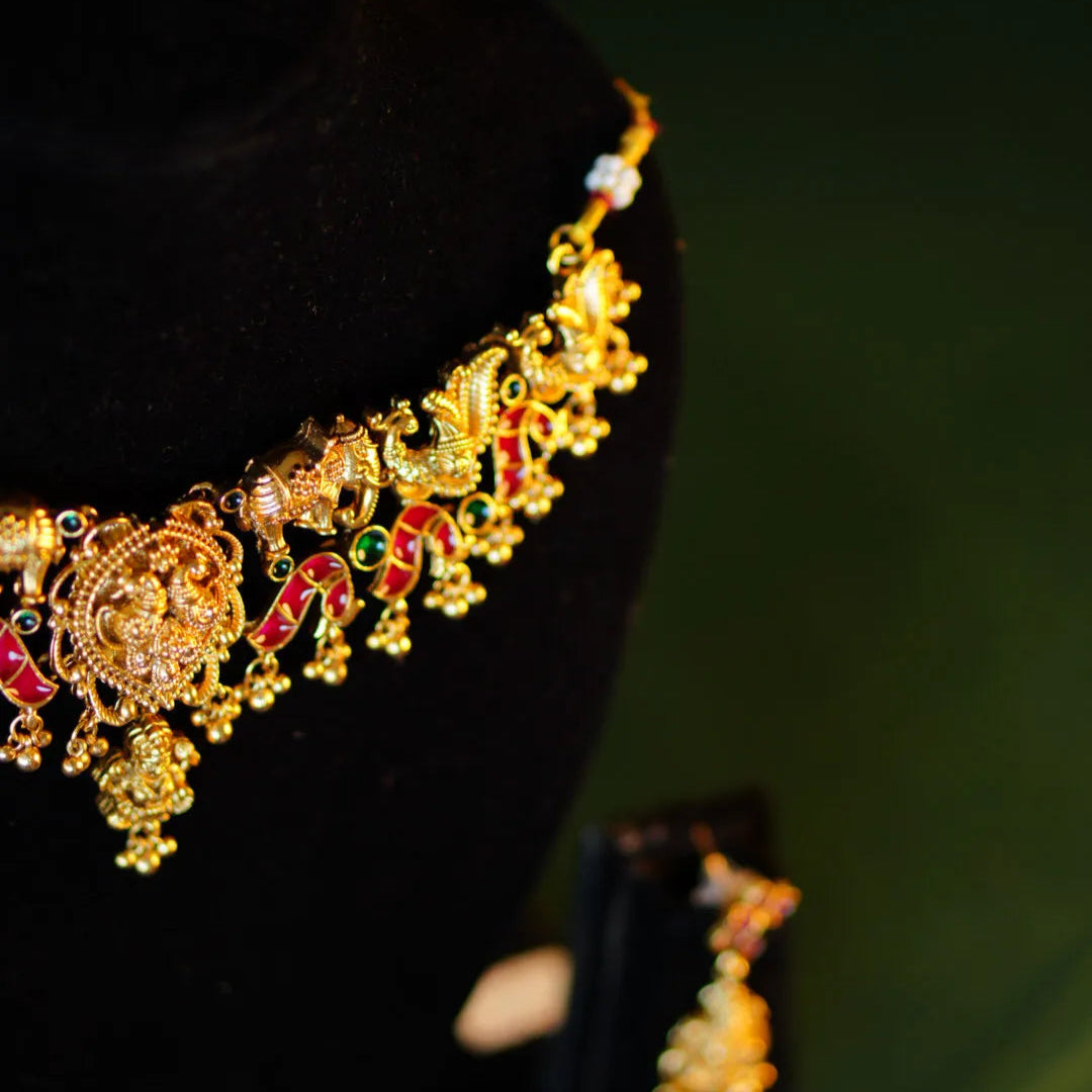 Gold necklace with red and green stones on a black stand against a dark background