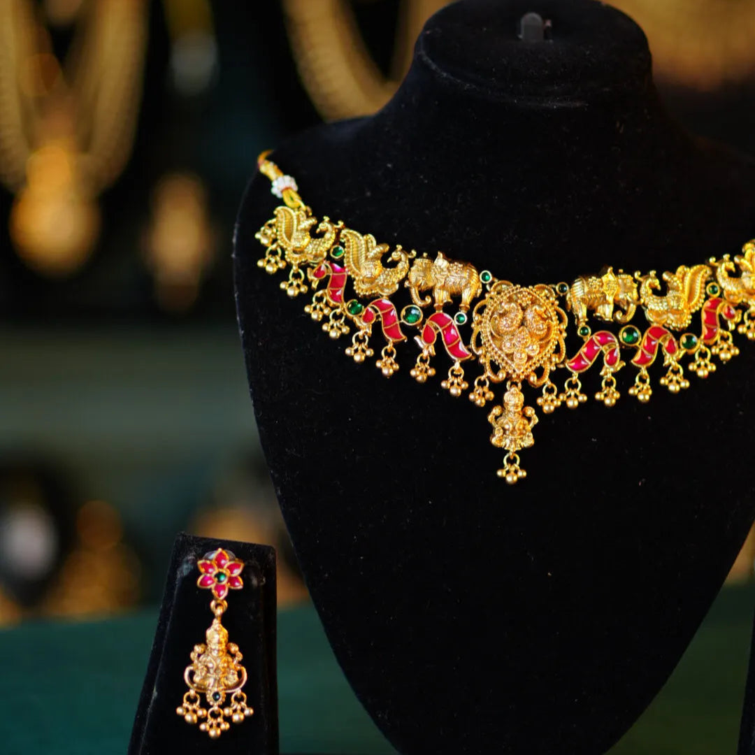 Gold necklace with red and green accents on a black mannequin bust against a blurred jewelry store background.