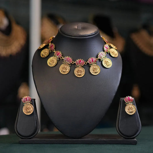 Gold necklace with pink flowers and matching earrings on a black stand against a blurred jewelry store background.