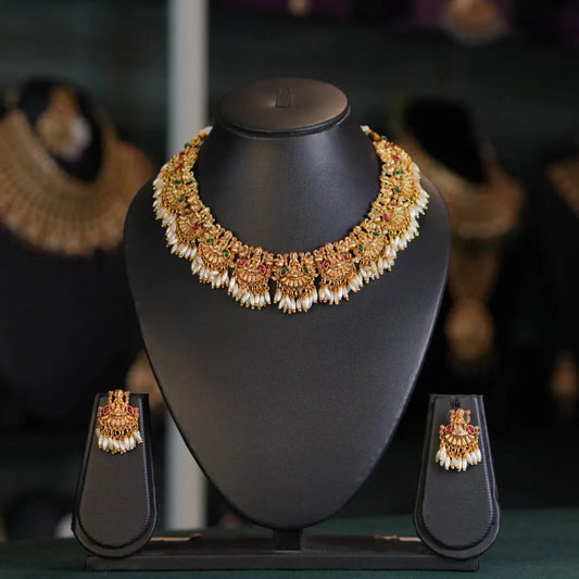 Gold necklace and earrings on a black mannequin bust with a blurred jewelry store background.