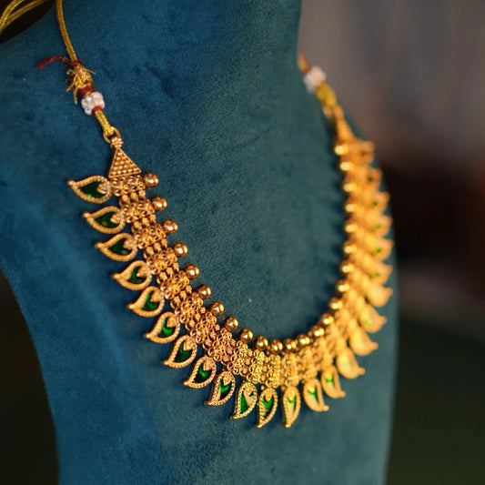 Gold necklace with green gemstones on a blue mannequin