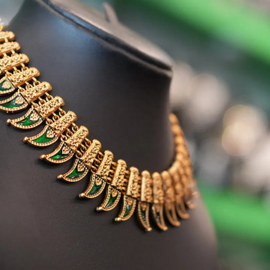 Gold necklace with green accents on a black mannequin against a blurred background