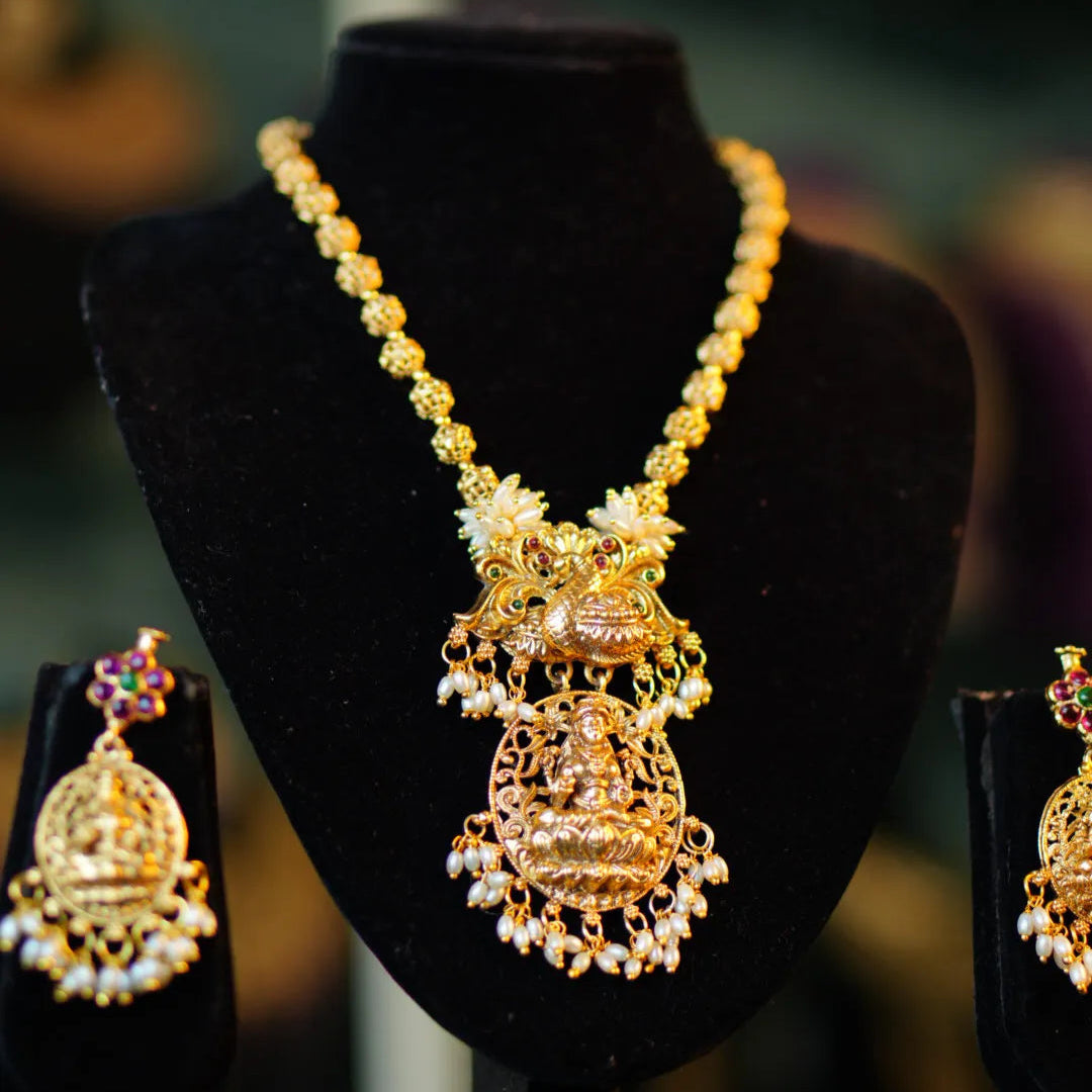 Gold necklace and earrings on a black stand with a blurred background
