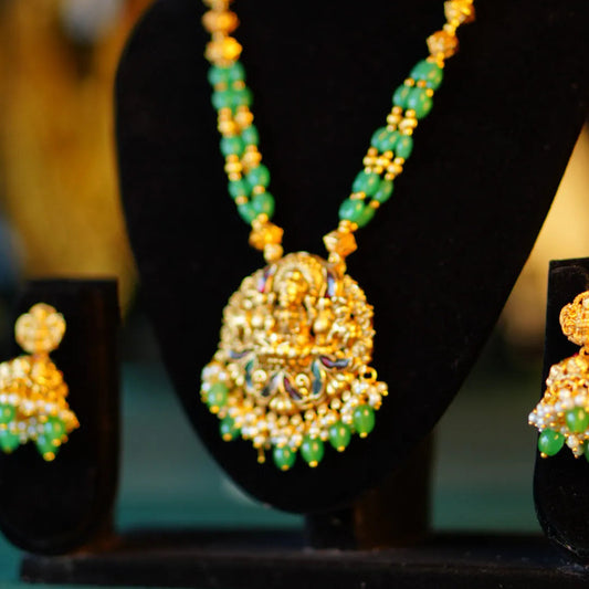 Gold and green necklace with matching earrings on a black stand.