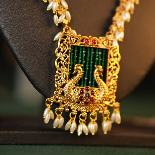 Gold necklace with a green pendant and pearl accents on a dark background