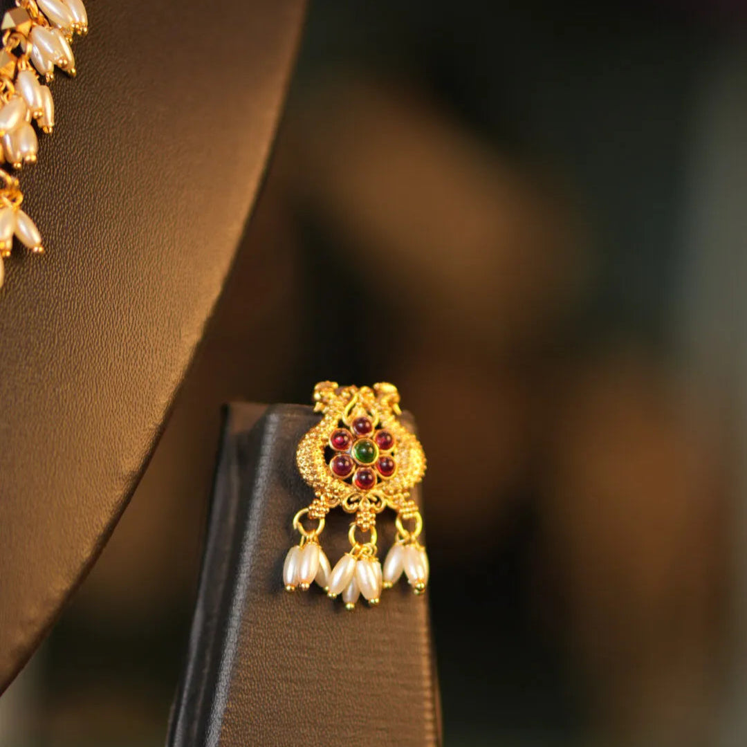 Gold earring with red stones and pearl-like beads on a brown stand