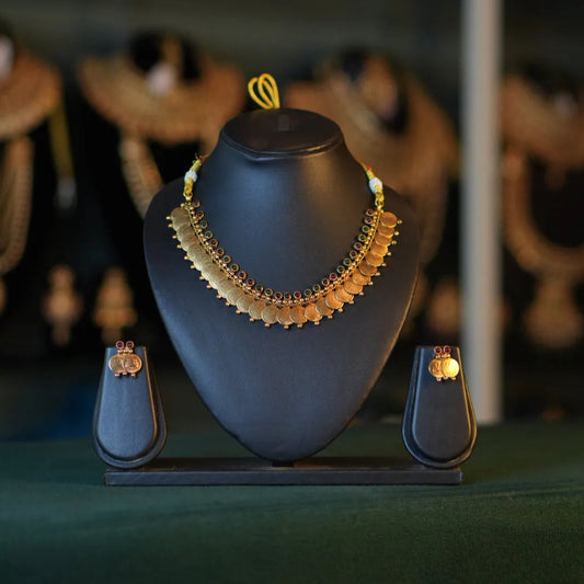 Gold necklace on a black mannequin bust with earrings on either side, against a dark background.