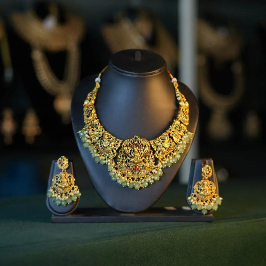Gold necklace and earrings on a dark stand with a blurred jewelry store background